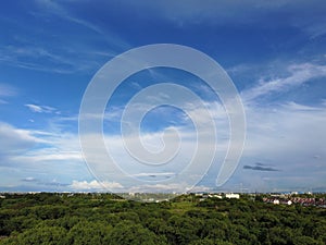 Aerial view of lush green field in a rural area under blue cloudy sky with buildings in background