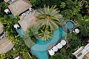 Aerial view of luxury hotel with straw roof villas and swimming pools in tropical jungle and palm trees. Luxurious villa