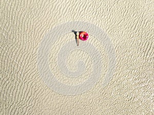 Aerial view of lying slim woman with swimming ring, sandy beach