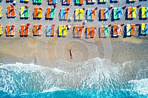 Aerial view of lying woman on the beach with colorful chaise-lounges. Beautiful young woman on the sea at sunset in Oludeniz