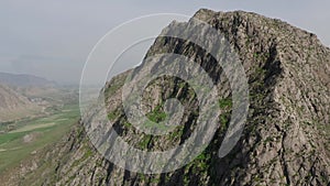 Aerial view of majestic rock with green vegetation against misty valley at background. Splendid wild nature in highlands
