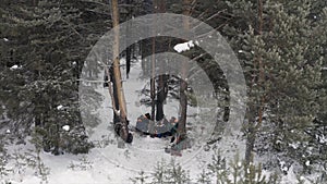 Aerial view of male hunters sitting and having a rest around the fire in a winter forest. Clip. Group of people getting
