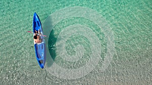 Aerial view of man in floating kayak. kayaking out from beach on clear blue sea. right side copy space. water sports and summer