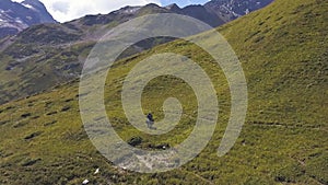 Aerial view of a man riding a horse on a green moountain slope. Clip. Beautiful summer day, mountain range, cloudy sky