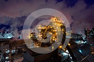 Aerial view of metallurgical plant blast furnace at night with smokestacks and fire blazing out of pipe. Industrial panoramic