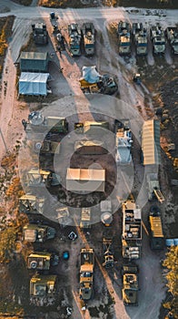 Aerial view of a military convoy arrayed on a remote dirt road at dusk, showcasing a systematic arrangement of tents and