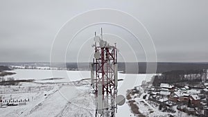 Aerial view mobile tower with antennas dish for mobile wave in winter village. Drone view communication tower with