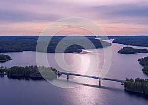 Aerial view of modern bridge with cars across blue lake Saimaa at summer sunset time. Beautiful sky with clouds. Finland