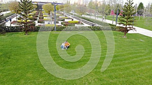 Aerial view of modern recreation park. Couple is sitting on green lawn among unique trees and plants. Geometric pattern