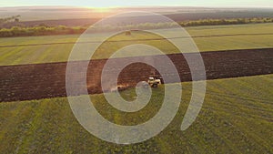Aerial view modern red tractor on the agricultural field on sunset time. Tractor plowing land and cultivating field.