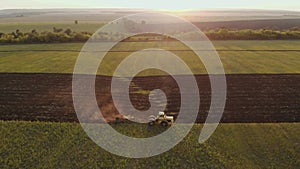 Aerial view modern red tractor on the agricultural field on sunset time. Tractor plowing land and cultivating field.