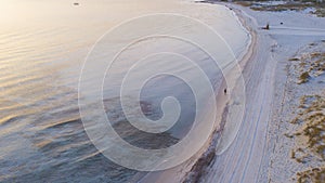 Aerial view of morning light at the beach with calm sea water and people walking on the sand for active outdoor leisure. Concept