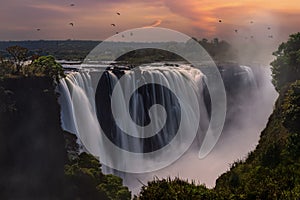 Aerial view of Mosi-Oa-Tunya Falls waterfall in Zambia during sunset with birds flying around photo