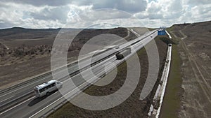 Aerial view of a motorway with driving cars and large cargo truck. Shot. Road built along endless fields on cloudy sky