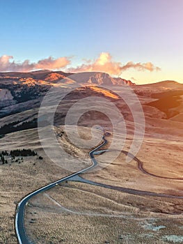 Aerial view of mountain road and beautiful orange sunrise in autumn. Top view of mountain landscape