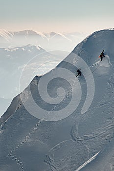 aerial view of mountain slope covered with snow along which groups of skiers climb