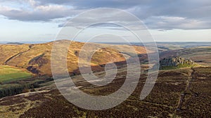 An aerial view of a mountain valley with grassy and stony slopes, trees and mountain range summits under a majestic blue sky and