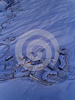 Aerial view of mountain village chalets illuminated with night street lights along switchbacks curvy road at twilight on