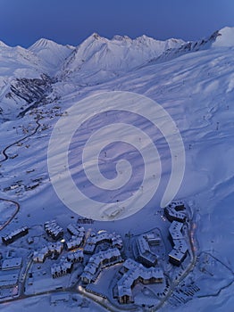 Aerial view of mountain village chalets illuminated with night street lights along switchbacks curvy road at twilight on