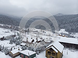 Aerial view of a Mountain Village with Hills Covered in Snow and Pine Forest in Winter. Yaremche, Ukraine. Flying over