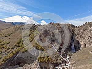Aerial view of mountain waterfall and Mount Elbrus. View of snowy white cloudless peak of Mount Elbrus. Stormy river