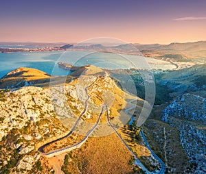 Aerial view of mountains, road, trees, blue sea at sunset