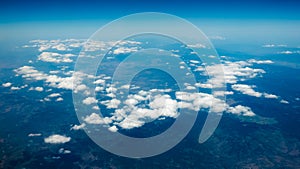 Aerial view of mountains under the clouds and blue sky. View from a plane window. Beautiful landscape