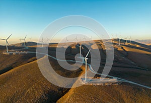 Aerial view of multiple wind turbines standing on a hill and generating electricity at sunrise