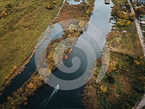 Aerial view of narrow river with small boat sailing by surrounded by autumn meadows - enjoy water sports concept