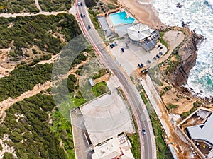 Aerial view of a narrow road with vehicles driving along the wild south coastline facing the Atlantic Ocean wit crispy waves