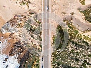 Aerial view of a narrow road with vehicles driving along the wild south coastline facing the Atlantic Ocean wit crispy waves