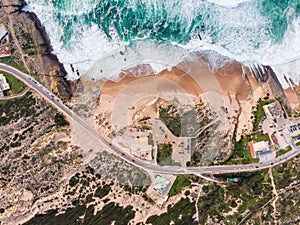 Aerial view of a narrow road with vehicles driving along the wild south coastline facing the Atlantic Ocean wit crispy waves