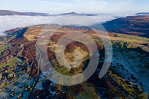 Aerial view of a narrow, winding mountain road on a hillside above a fog filled valley