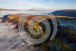 Aerial view of a narrow, winding mountain road on a hillside above a fog filled valley