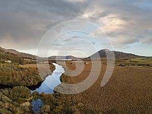 Aerial view, Nature landscape, Small river flows by a field, Mountains in the background, Cloudy sky, Connemara, County Galway,