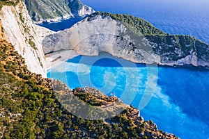 Aerial view of Navagio Beach - Shipwreck beach - on Zakynthos Island, Greece. Tourists on cliff edge enjoy view on