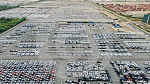 Aerial view of new cars stock at factory parking lot. Above view many cars parked in a row. Automotive industry. Logistics and