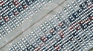 Aerial view of new cars stock at factory parking lot. Above view many cars parked in a row. Automotive industry. Logistics and
