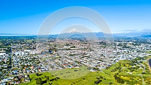 Aerial view on a New Plymouth residential suburb surrounded by green meadow with Mount Taranaki on the background. New Zealand