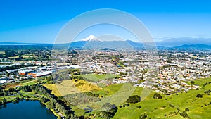 Aerial view on a New Plymouth residential suburb surrounded by green meadow with Mount Taranaki on the background. New Zealand