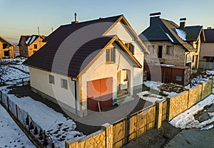Aerial view of new residential house cottage and attached garage with shingle roof on fenced yard on sunny winter day in modern