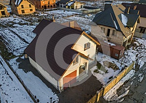 Aerial view of new residential house cottage and attached garage with shingle roof on fenced yard on sunny winter day in modern