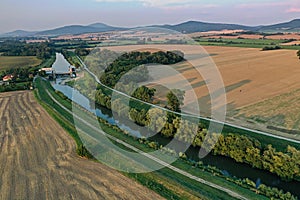 Letecký pohľad na rieku Nitra tečúcu v nížinách západného Slovenska, na ktorej je postavená malá vodná elektráreň