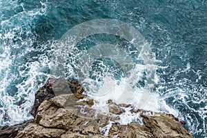 Aerial view of ocean wave crashing on rocky cliff with white spray and foam on deep blue sea water after storm