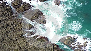 Aerial view of ocean wave crashing on rocky cliff with white spray and foam on deep blue sea water after storm