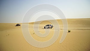 Aerial view on Off-road adventure with SUV in Arabian Desert at sunset with Dubai skyline or cityscape. Desert touring