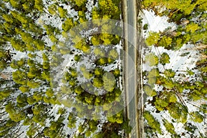 Aerial view of old asphalt road in the spring forest. Snow melts on the side of the road