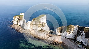 An aerial view of the Old Harry Rocks with crystal clear water, white cliffs and speed boat in the background under a hazy sky