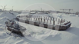 Aerial view of an old pier and a moored rusty ship on a snow covered shore. Clip. Winter landscape of an abandoned pier