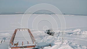 Aerial view of an old pier and a moored rusty ship on a snow covered shore. Clip. Winter landscape of an abandoned pier